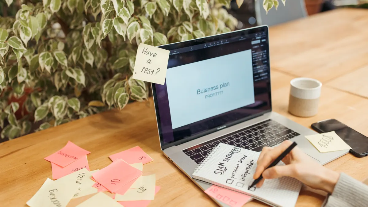 Desk with laptop, sticky notes, and a hand writing notes